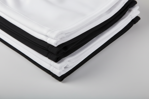 polyester, cotton shorts in white and black stacked on each other, close up, somewhat folded. close up shot in an angle to show quality of the pants. make sure the shorts, pants are blank